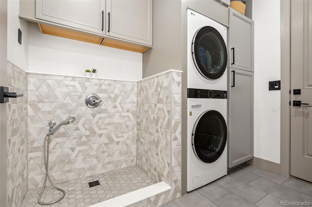 washroom with stacked washing machine and dryer, light tile patterned flooring, and cabinet space