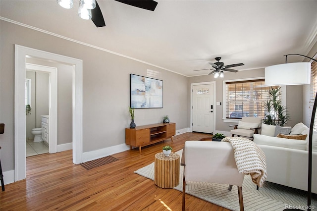 living room featuring baseboards, ceiling fan, ornamental molding, and wood finished floors