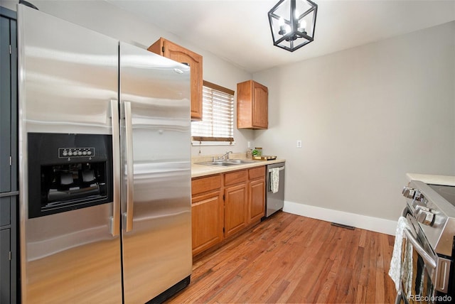 kitchen with light wood finished floors, baseboards, appliances with stainless steel finishes, light countertops, and a sink