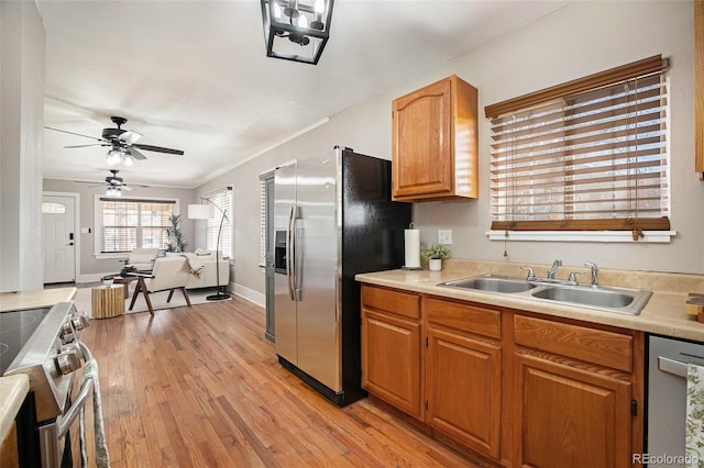 kitchen with a sink, light countertops, ornamental molding, appliances with stainless steel finishes, and light wood-type flooring