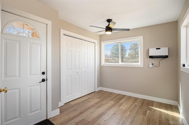 unfurnished bedroom featuring light wood finished floors, a closet, a ceiling fan, a wall mounted air conditioner, and baseboards