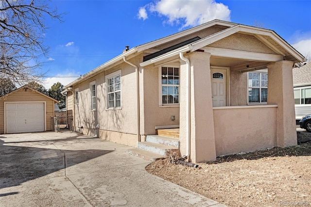 view of front facade with an outdoor structure, driveway, a detached garage, and stucco siding