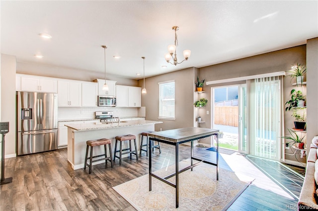 kitchen with dark wood finished floors, a kitchen island with sink, white cabinets, appliances with stainless steel finishes, and backsplash