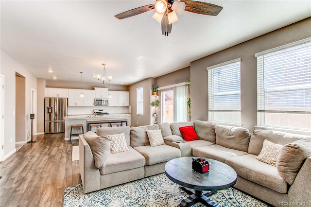 living area featuring ceiling fan with notable chandelier, light wood-type flooring, and baseboards