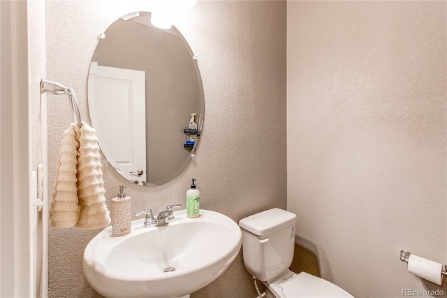 half bath with toilet, a textured wall, and a sink