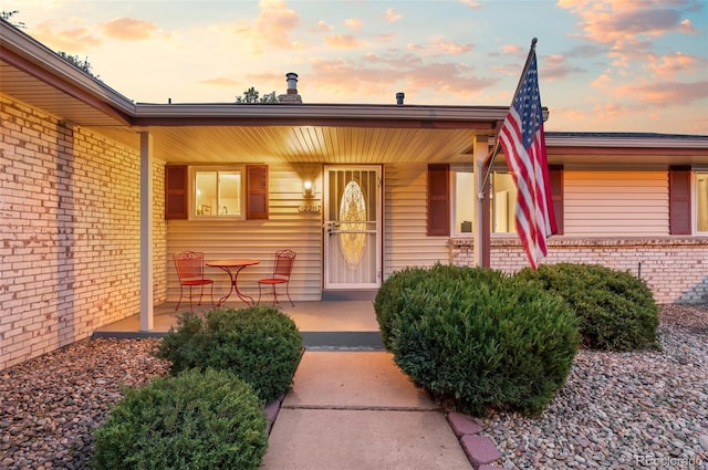 exterior entry at dusk featuring covered porch and brick siding