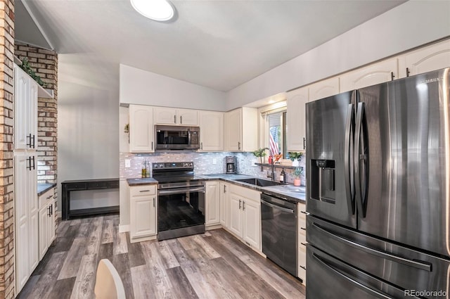 kitchen featuring lofted ceiling, stainless steel appliances, a sink, decorative backsplash, and dark countertops