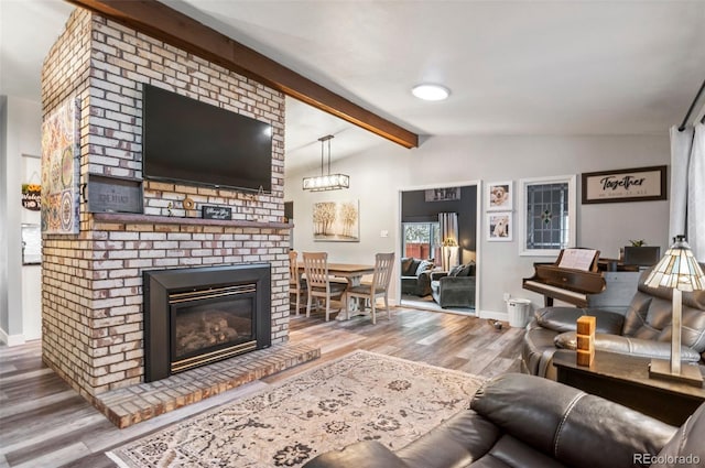 living room featuring vaulted ceiling with beams, a brick fireplace, baseboards, and wood finished floors