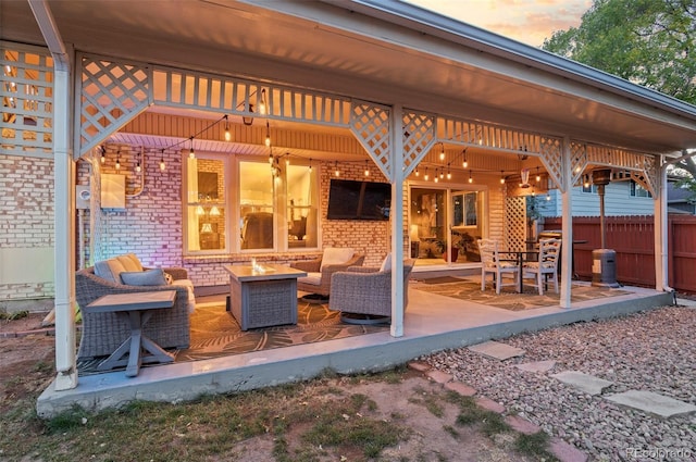 patio terrace at dusk featuring an outdoor living space with a fire pit and fence