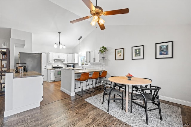 dining area with ceiling fan with notable chandelier, vaulted ceiling, and dark hardwood / wood-style flooring