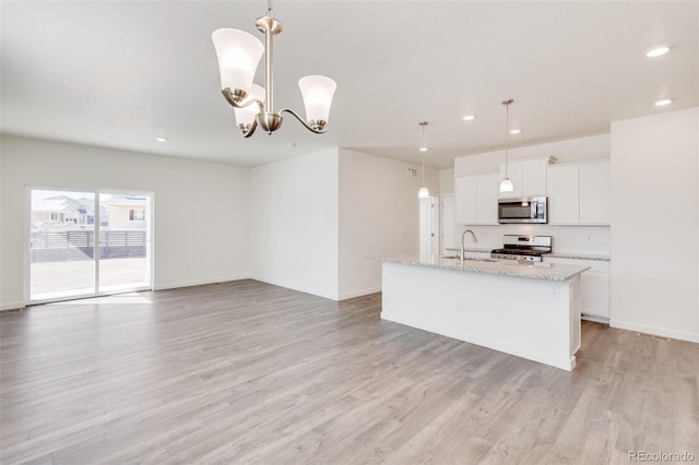 kitchen featuring pendant lighting, sink, stainless steel appliances, an island with sink, and white cabinets