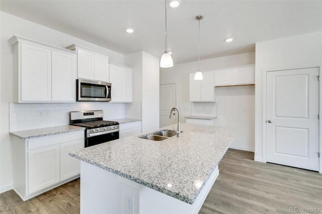 kitchen with sink, white cabinetry, hanging light fixtures, stainless steel appliances, and a center island with sink