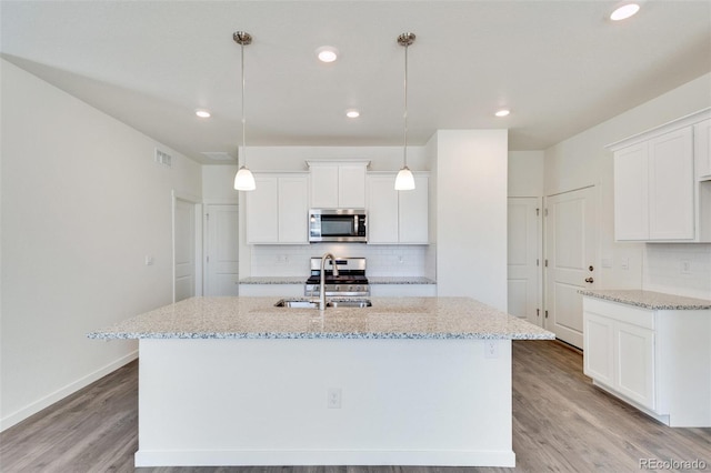 kitchen featuring a kitchen island with sink, sink, decorative light fixtures, and white cabinets