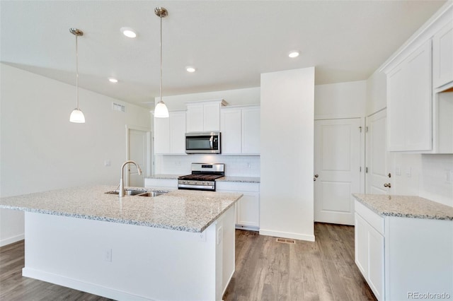 kitchen featuring appliances with stainless steel finishes, sink, white cabinets, hanging light fixtures, and a kitchen island with sink