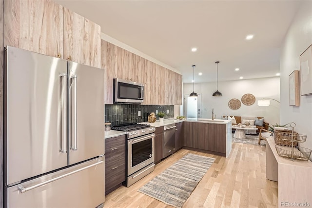 kitchen with kitchen peninsula, hanging light fixtures, stainless steel appliances, light hardwood / wood-style floors, and backsplash