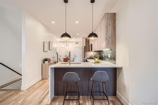 kitchen featuring kitchen peninsula, decorative light fixtures, a breakfast bar, backsplash, and sink