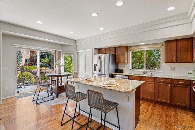 kitchen with light wood-type flooring, a kitchen island, appliances with stainless steel finishes, light stone countertops, and decorative backsplash