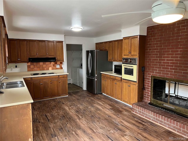 kitchen featuring sink, white appliances, a brick fireplace, dark hardwood / wood-style flooring, and independent washer and dryer