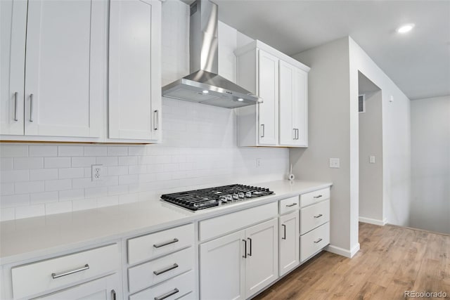 3443 N Gold Bug Ct, Aurora, CO 80019 - kitchen featuring stainless steel gas stovetop, decorative backsplash, white cabinets, light wood-style flooring, and wall chimney exhaust hood