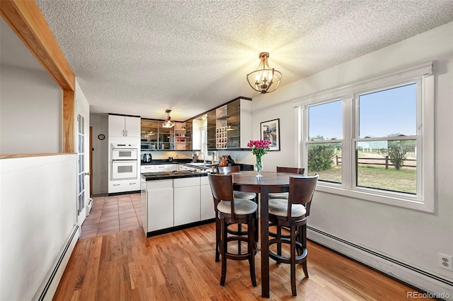 kitchen with dark countertops, hanging light fixtures, an inviting chandelier, baseboard heating, and white cabinetry