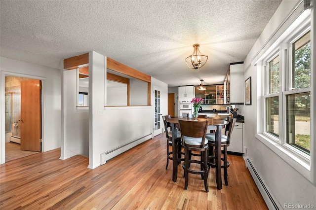 dining space featuring a healthy amount of sunlight, a baseboard radiator, and light wood-style floors