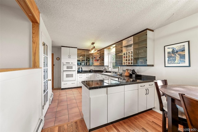 kitchen featuring double oven, a peninsula, a sink, white cabinetry, and pendant lighting
