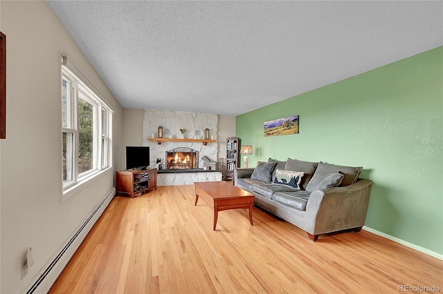 living room with a textured ceiling, a baseboard heating unit, wood finished floors, and a stone fireplace