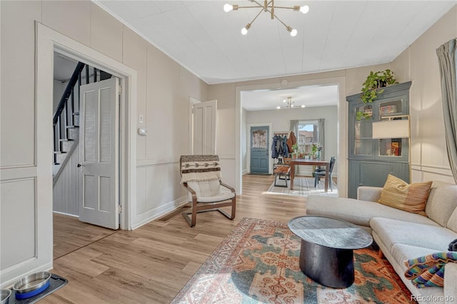 living area featuring light wood-style flooring, a notable chandelier, stairs, crown molding, and a decorative wall