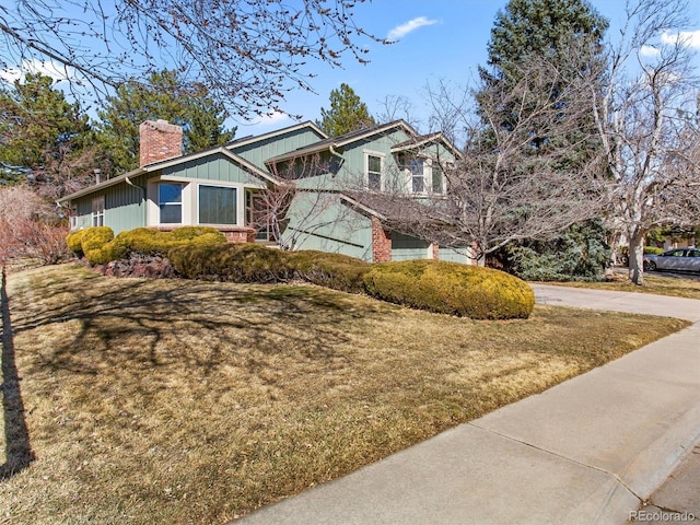 view of front of house featuring an attached garage, brick siding, concrete driveway, a front lawn, and a chimney