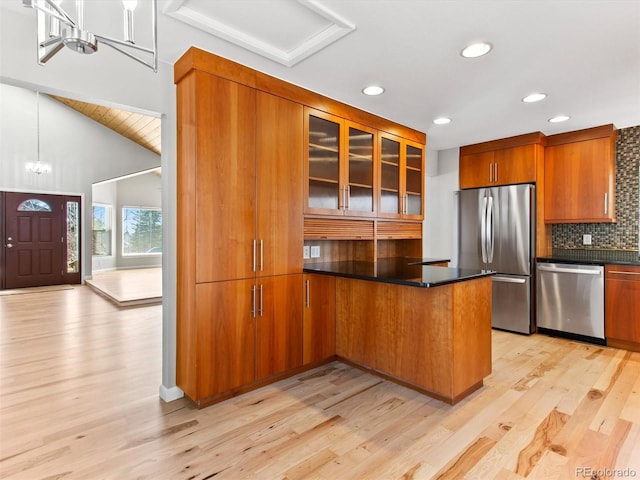 kitchen with brown cabinetry, dark countertops, appliances with stainless steel finishes, a peninsula, and a chandelier