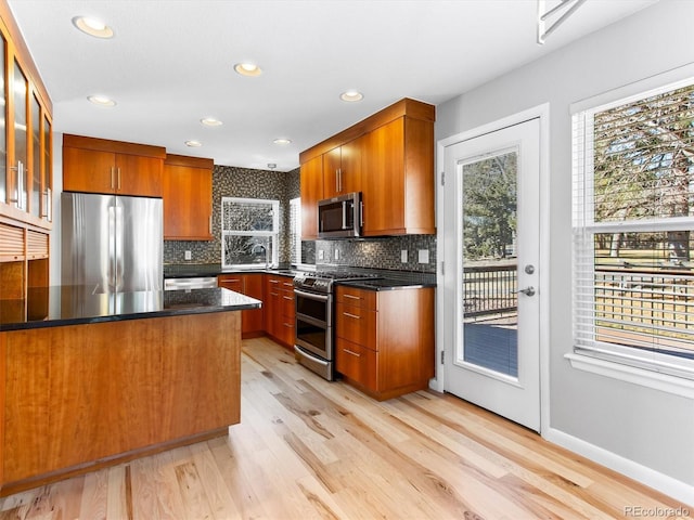 kitchen with light wood-type flooring, backsplash, stainless steel appliances, and a wealth of natural light