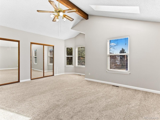 unfurnished bedroom with vaulted ceiling with skylight, carpet floors, visible vents, baseboards, and multiple closets