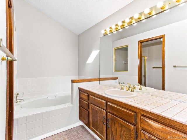 bathroom with a textured ceiling, tile patterned flooring, a garden tub, and vanity