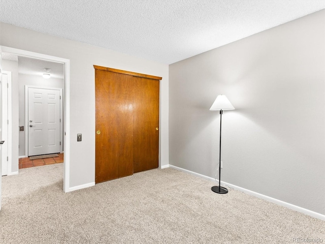 unfurnished bedroom with a closet, carpet flooring, a textured ceiling, and baseboards