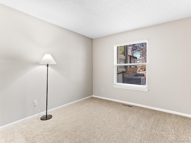 empty room featuring a textured ceiling, carpet flooring, visible vents, and baseboards