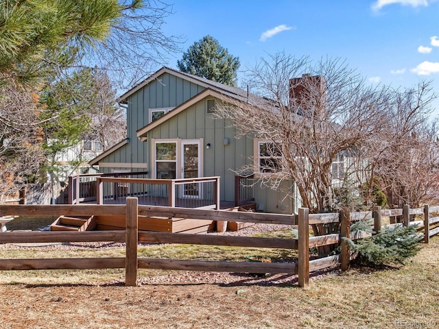 view of front facade with a chimney, fence, board and batten siding, and a wooden deck