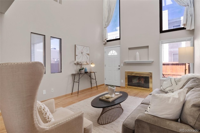 living area with light wood finished floors, a glass covered fireplace, a towering ceiling, and baseboards