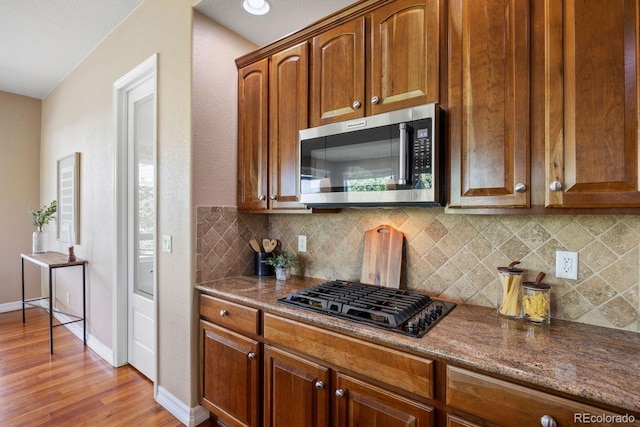 7472 Iridium Way, Castle Rock, CO 80108 - kitchen featuring stainless steel microwave, black gas cooktop, tasteful backsplash, and light wood-type flooring