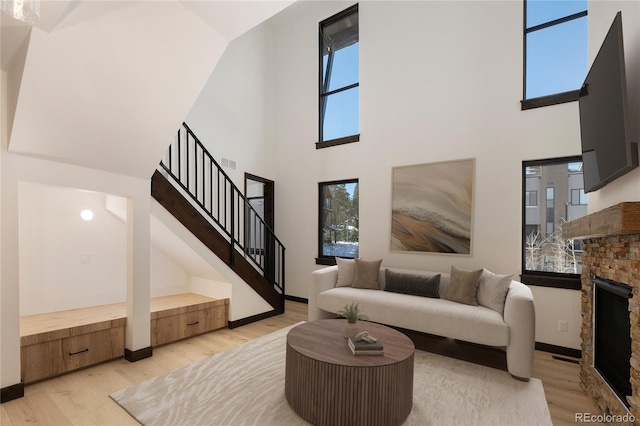 living room with a towering ceiling, a fireplace, and light wood-type flooring