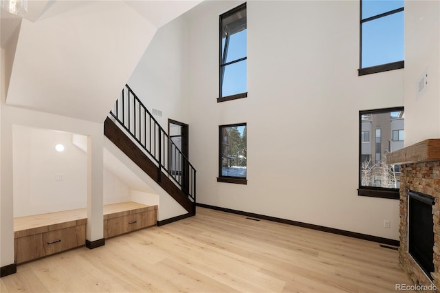 unfurnished living room with a towering ceiling, a fireplace, and light wood-type flooring