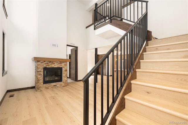 staircase featuring wood-type flooring, a stone fireplace, and a towering ceiling