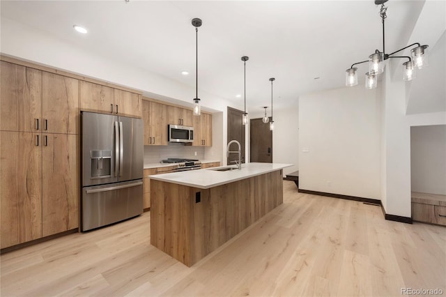 kitchen with an island with sink, appliances with stainless steel finishes, backsplash, and decorative light fixtures