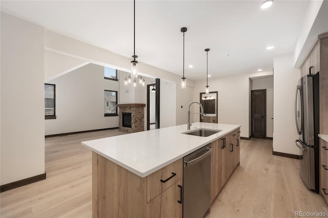 kitchen featuring sink, decorative light fixtures, an island with sink, stainless steel appliances, and a fireplace