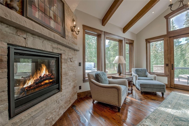 sitting room with a stone fireplace, beamed ceiling, plenty of natural light, and wood-type flooring