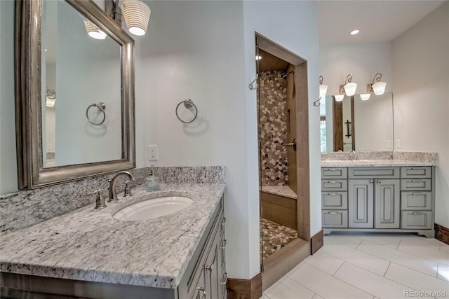 bathroom featuring two vanities, a tile shower, and a sink