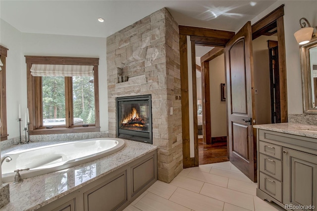 full bath featuring tile patterned floors, vanity, a garden tub, and a fireplace