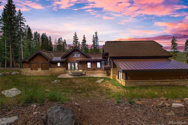 back of property at dusk with a patio area, stone siding, metal roof, and a standing seam roof