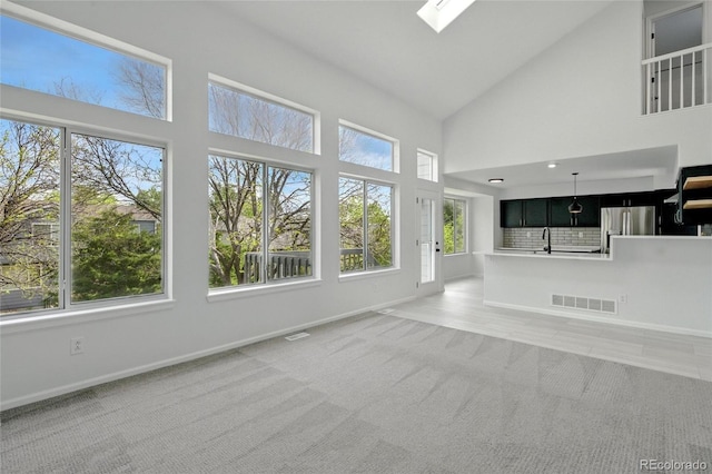unfurnished living room with baseboards, light colored carpet, high vaulted ceiling, a skylight, and a sink