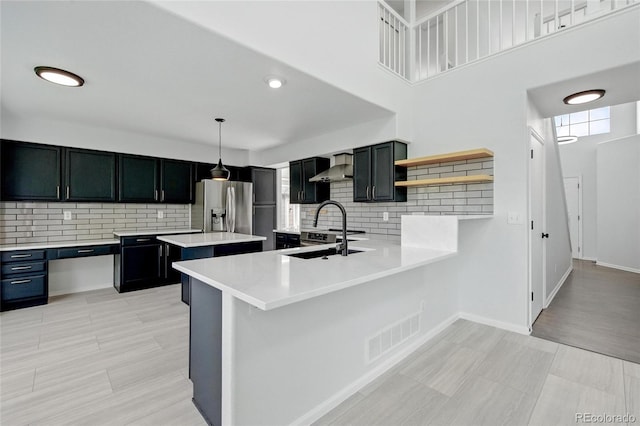 kitchen featuring stainless steel refrigerator with ice dispenser, wall chimney exhaust hood, light countertops, and backsplash