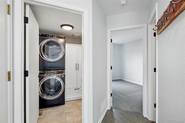 clothes washing area featuring stacked washer / dryer, cabinet space, and baseboards